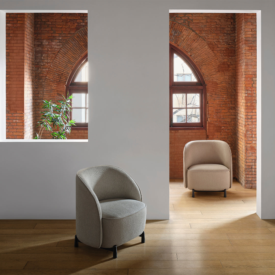 Light grey upholstered chair with subtle texture set against rustic brick walls and warm wooden flooring.