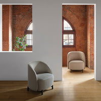 Light grey upholstered chair with subtle texture set against rustic brick walls and warm wooden flooring.
