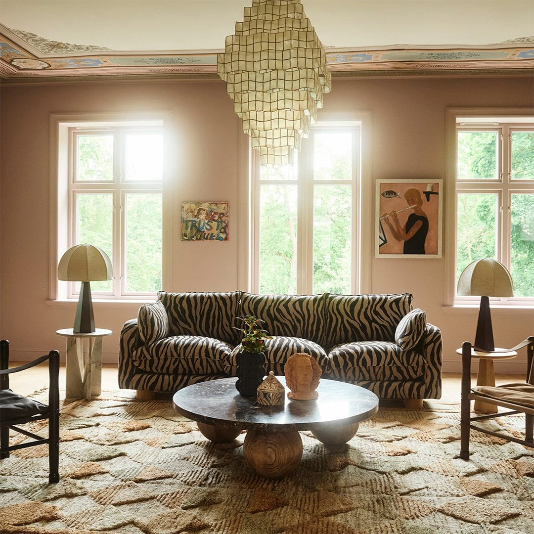 Zebra-patterned black and white couch in a pastel pink room with earthy tones from the rug and decor elements.