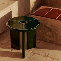 Glossy green side table with white accents, featuring a round top and three sleek legs, set against terracotta tiles.