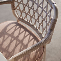 Beige woven chair with soft pink cushion and intricate diamond pattern casting shadows on a light surface.