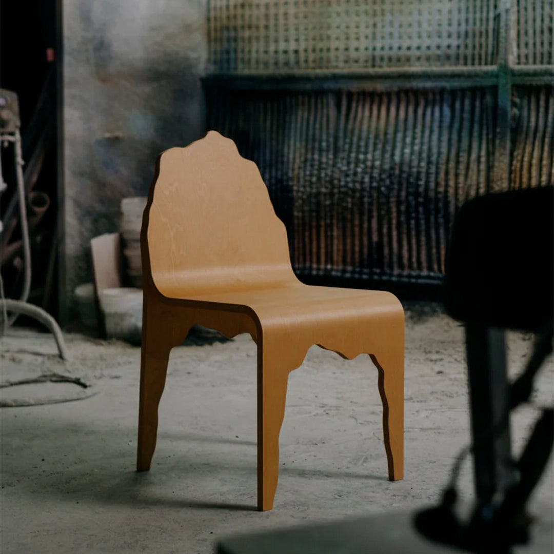 Minimalist natural wood chair with an organic, flowing silhouette against a rustic backdrop.