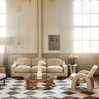 Beige sofa with textured fabric, geometric cream and brown rug, wood accents, and soft pastel wall art.