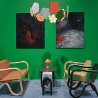"Bold green walls, abstract art in dark tones, and a vibrant orange decorative piece contrast against warm wood furniture."