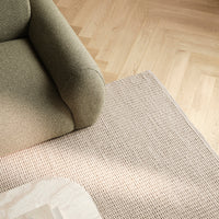 Olive green sofa and beige textured rug on light wooden flooring, creating a warm, modern aesthetic.