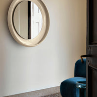Beige circular mirror against a light wall, with a soft blue chair and glass side table accents.