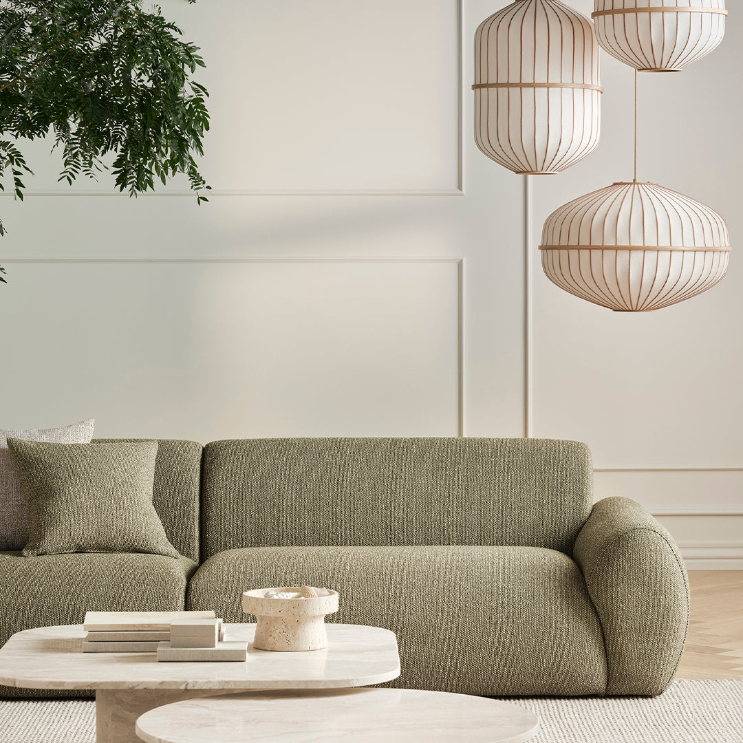 Textured olive green sofa with a soft pattern, complemented by light neutral shades and elegant hanging light fixtures.