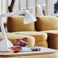White lamp with a curved shade, amber glass bowls, and mustard-colored curved sofa. Textured wood table surface.