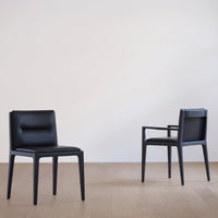 "Two sleek black chairs with smooth leather upholstery on a light wooden floor, minimalist design and modern style."