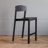 Black wooden chair with a minimalist design and smooth finish against a light grey wall and herringbone wood floor.