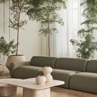 Green textured sofa with soft curves, paired with neutral ceramic vases on a light marble table.