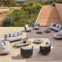 Modern outdoor seating set in soft gray fabric with black wicker accents and circular tables on a natural landscape.