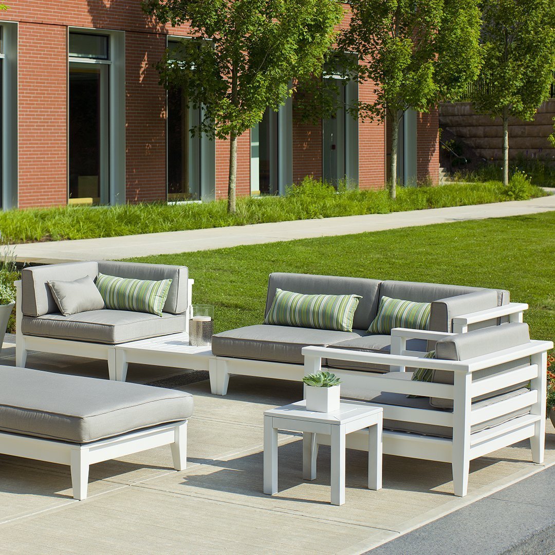 Gray outdoor sectional sofa with striped green and white cushions, set against a lush green lawn and modern architecture.