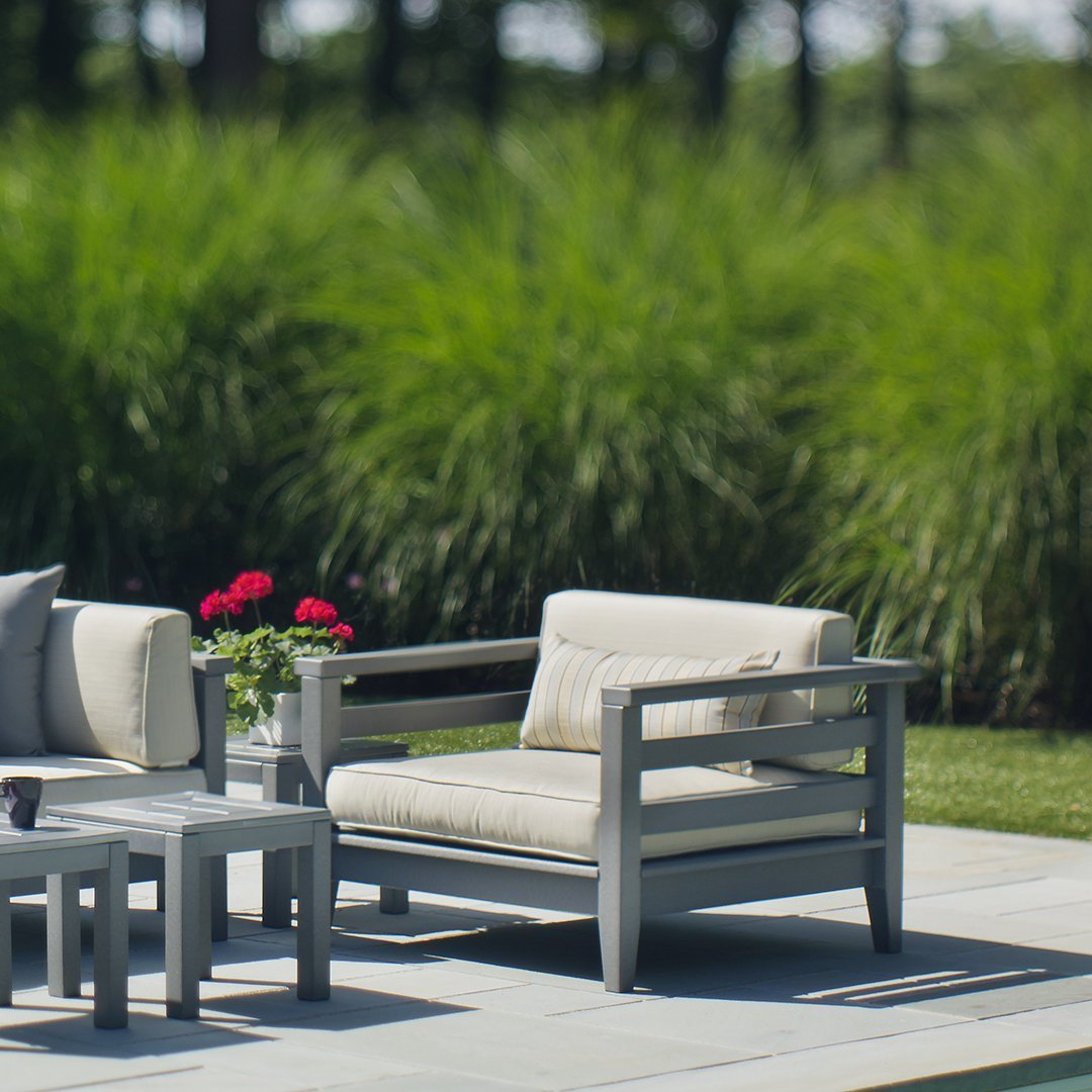 Light gray outdoor lounge chair with beige cushions, surrounded by lush green grass and vibrant red flowers.