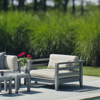 Light gray outdoor lounge chair with beige cushions, surrounded by lush green grass and vibrant red flowers.