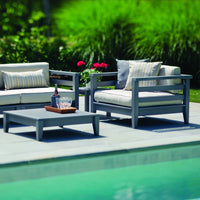 Modern gray patio furniture with striped cushions, set against lush green foliage and a shimmering pool.