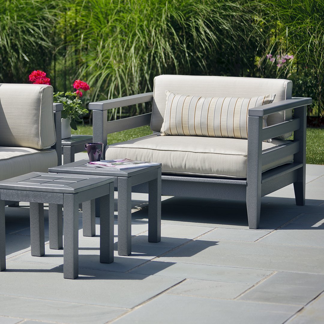 Light gray outdoor armchair with striped beige and yellow cushion, accompanied by a matching gray side table.