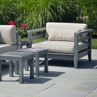 Light gray outdoor armchair with striped beige and yellow cushion, accompanied by a matching gray side table.