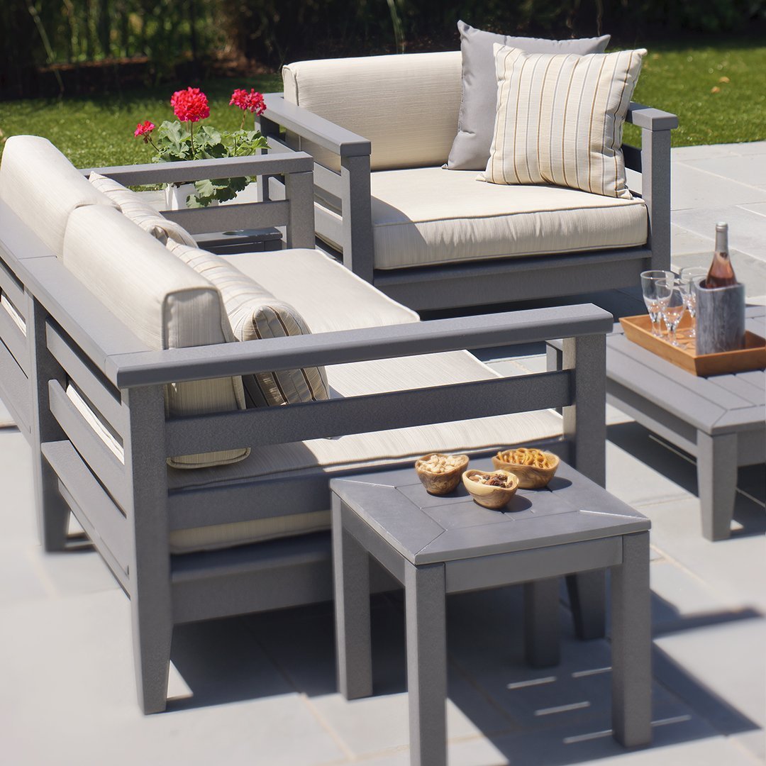 Modern gray outdoor seating set with cream cushions and striped accent pillows against a lush green backdrop.