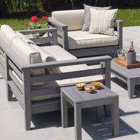 Modern gray outdoor seating set with cream cushions and striped accent pillows against a lush green backdrop.