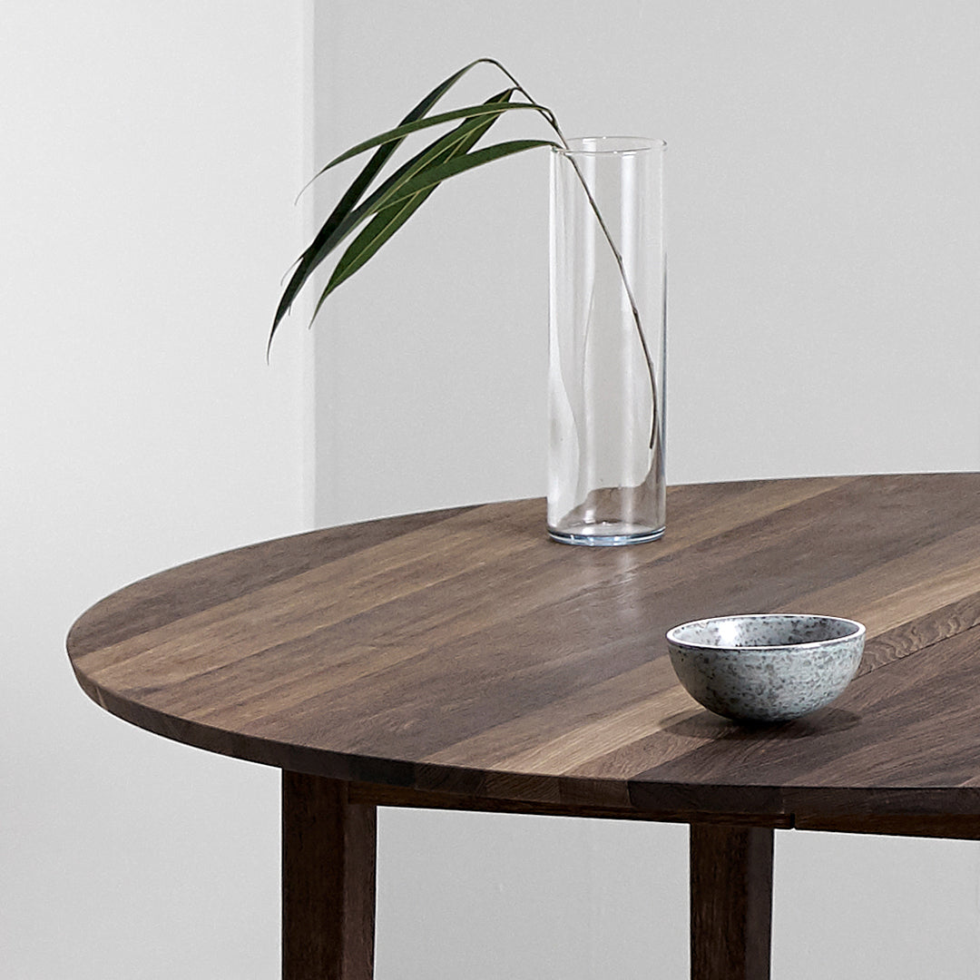 Circular wooden table in rich brown tones with striped patterns, complemented by a clear glass vase and a silver bowl.