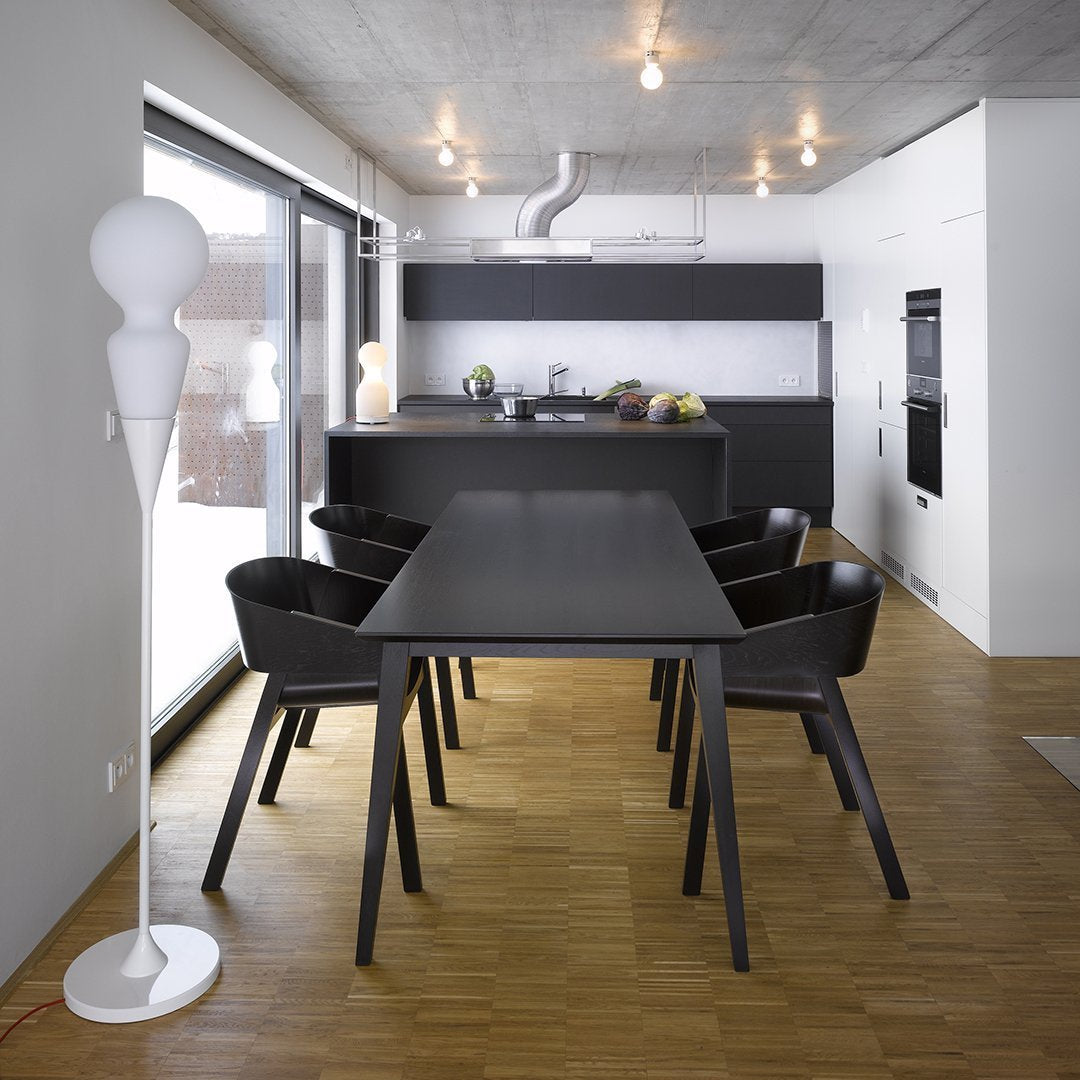 "Modern black dining table with matching chairs, wooden floor, and sleek white lamp under warm lighting."