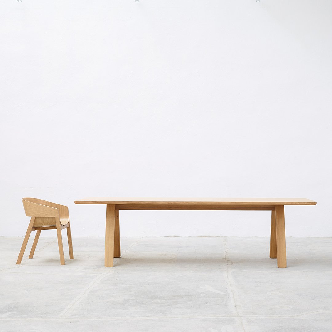 Light wood dining table and matching chair on a minimalist gray floor, showcasing natural grain patterns.