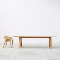 Light wood dining table and matching chair on a minimalist gray floor, showcasing natural grain patterns.