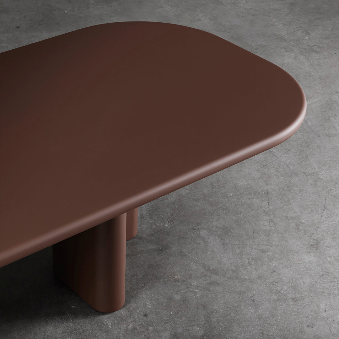Brown rounded table top with smooth finish and complementing cylindrical legs, set against a concrete background.