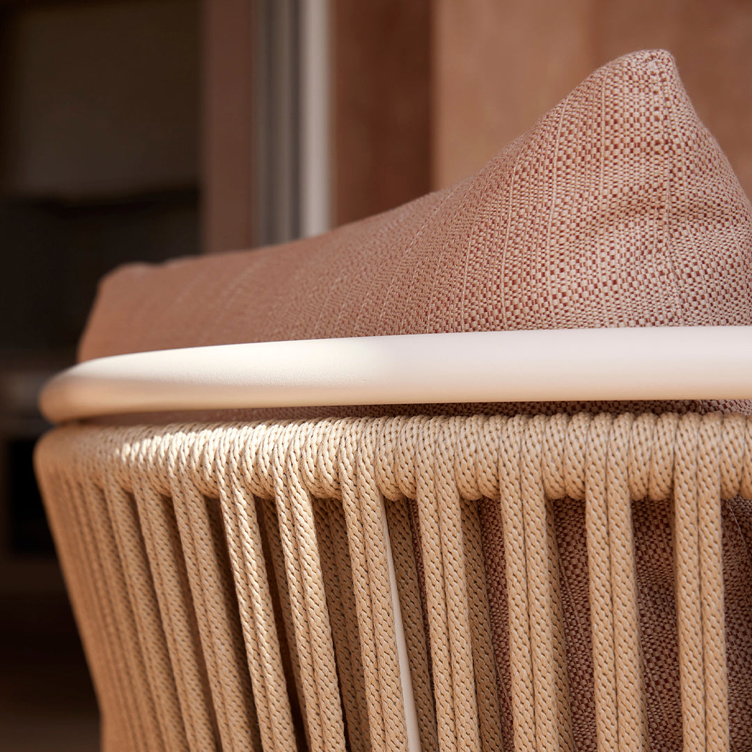 Beige woven seating with a textured, blush pillow, featuring subtle patterns and a sleek white trim.