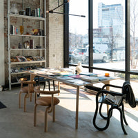 Modern workspace with wooden table, black and natural wooden chairs, vibrant book covers, and neutral brick wall.