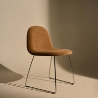 Brown upholstered chair with sleek chrome legs, set against a soft beige backdrop. Minimalist design and muted tones.