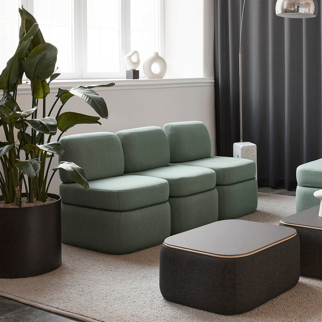 Soft green sofa with textured upholstery, paired with a dark gray coffee table and black planter, set in a neutral space.