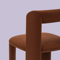 Brown upholstered chair against a soft lavender background, highlighting smooth textures and contemporary design.