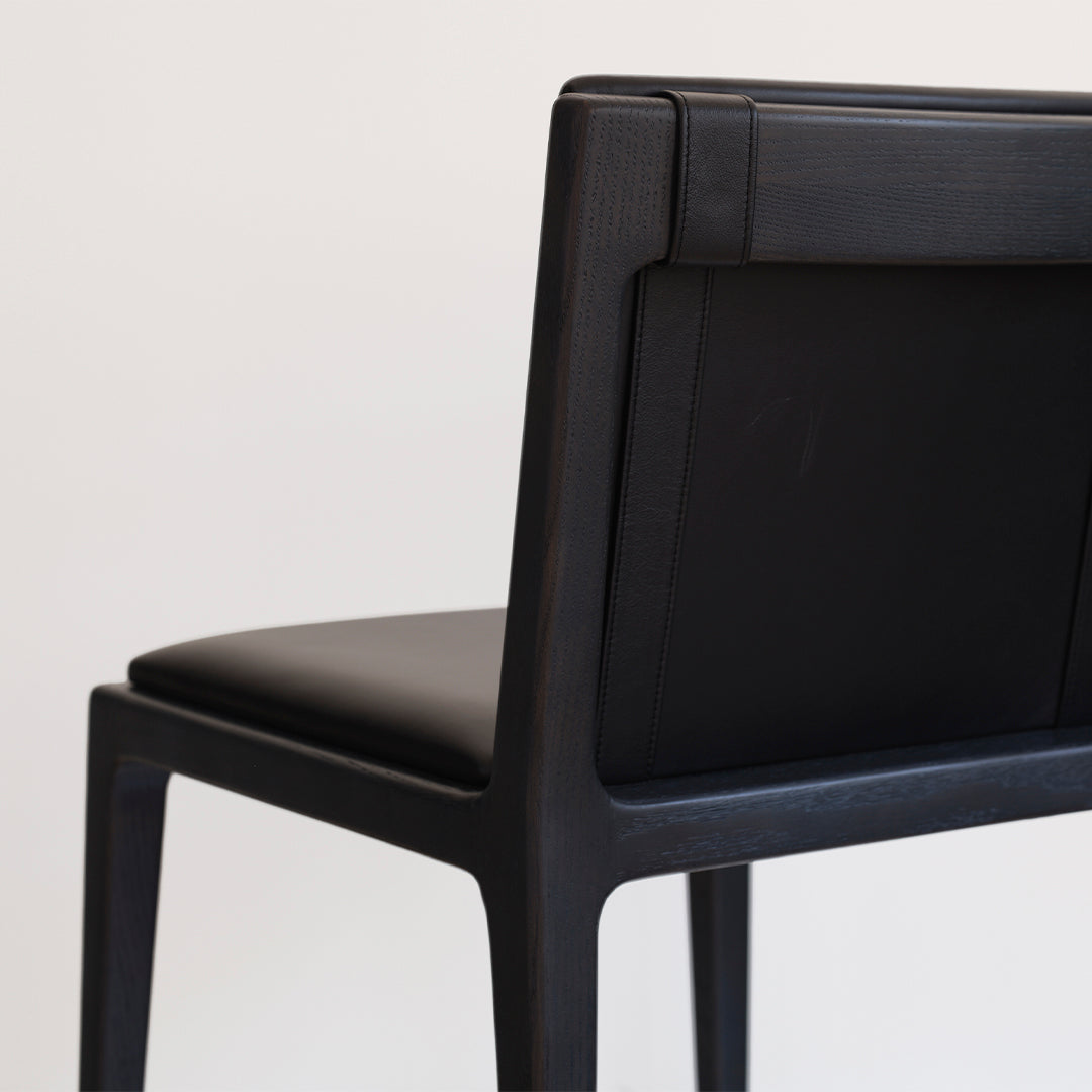 Black wooden chair with a smooth leather seat and back, featuring a sleek, minimalist design.