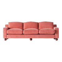 Soft coral velvet sofa with rounded cushions and dark wooden feet. Modern design ideal for cozy living spaces.