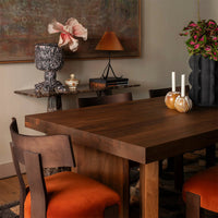 "Rich walnut table with orange velvet chairs, patterned vases, and a warm-toned backdrop create an inviting dining space."