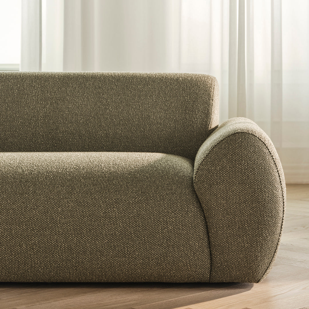 Textured olive green sofa fabric with a smooth, rounded armrest and subtle pattern. Bright, airy setting.