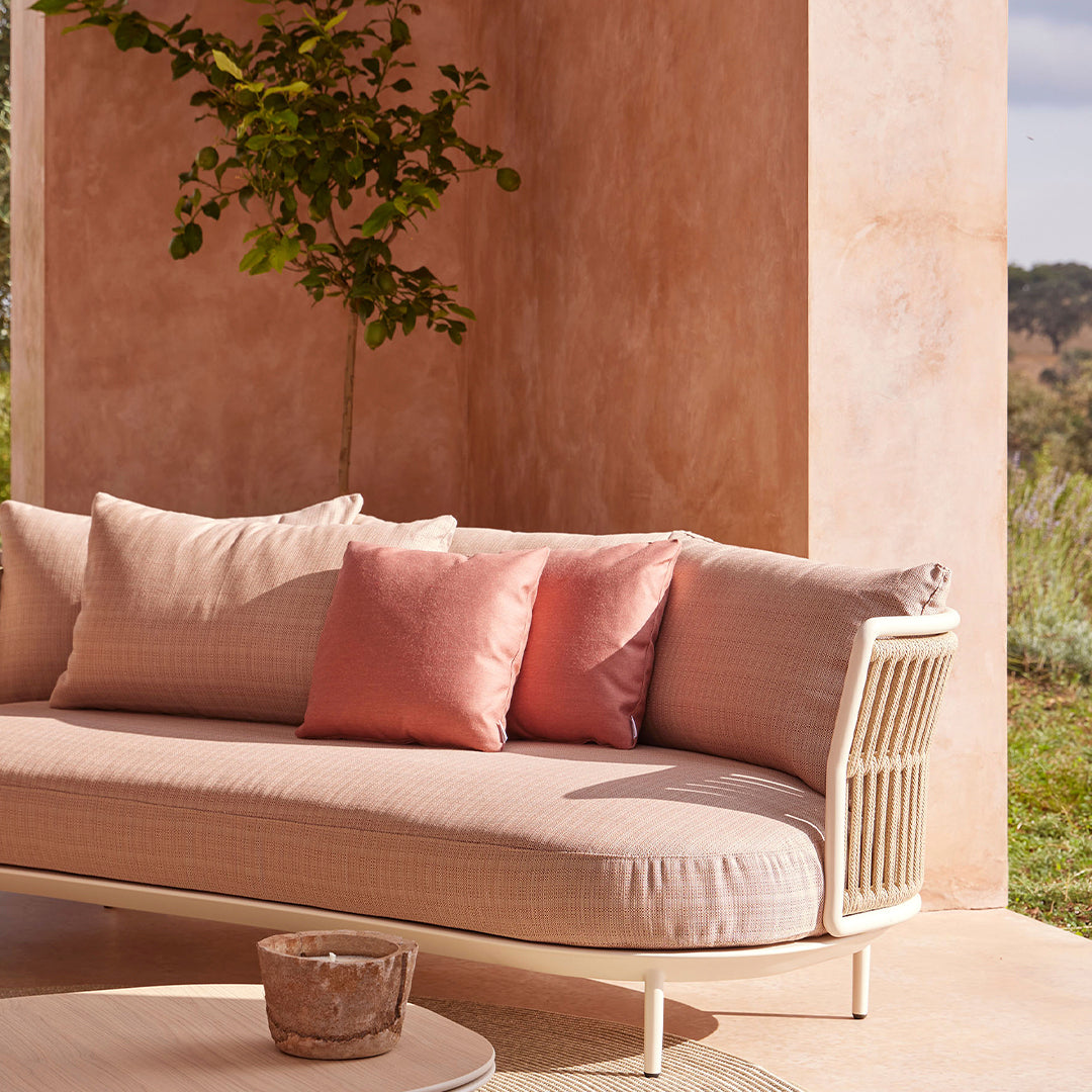 Soft pink sofa with cream cushions and coral accent pillows, set against a warm, textured peach wall.