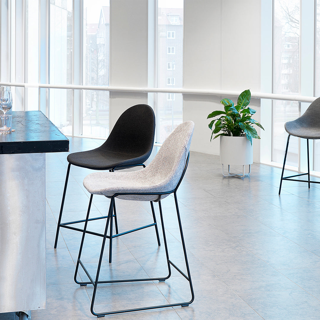 Two modern bar stools in black and light gray, featuring sleek lines and minimalist design, set against a bright backdrop.