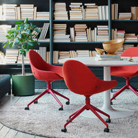 Red upholstered chairs with matching bases around a white table on a plush rug in a modern library setting.
