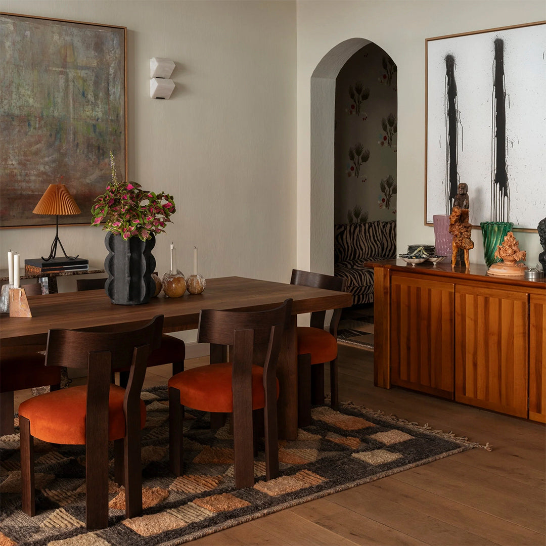 Modern dining area featuring earthy tones, orange accents, and a textured, geometric patterned area rug.