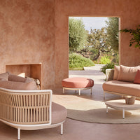 Modern living room with soft blush and peach tones, featuring a woven sectional sofa and round coffee table.