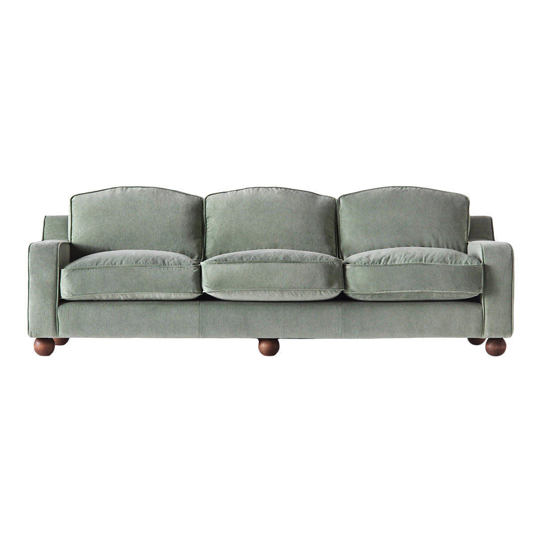 Green velvet sofa with three plush cushions and dark wooden legs, featuring a smooth, soft texture.