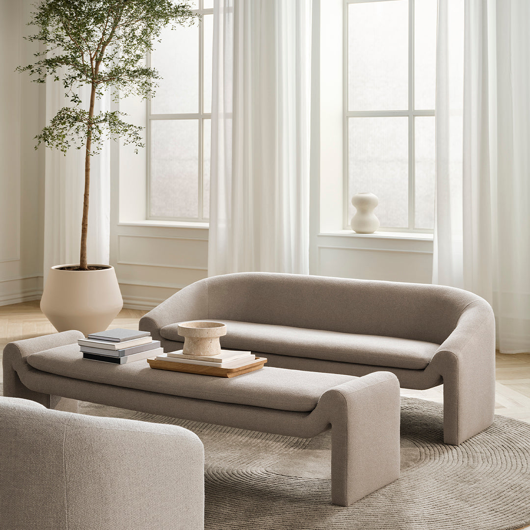Soft beige sofa and coffee table against a light, airy backdrop with warm white curtains and natural wood accents.
