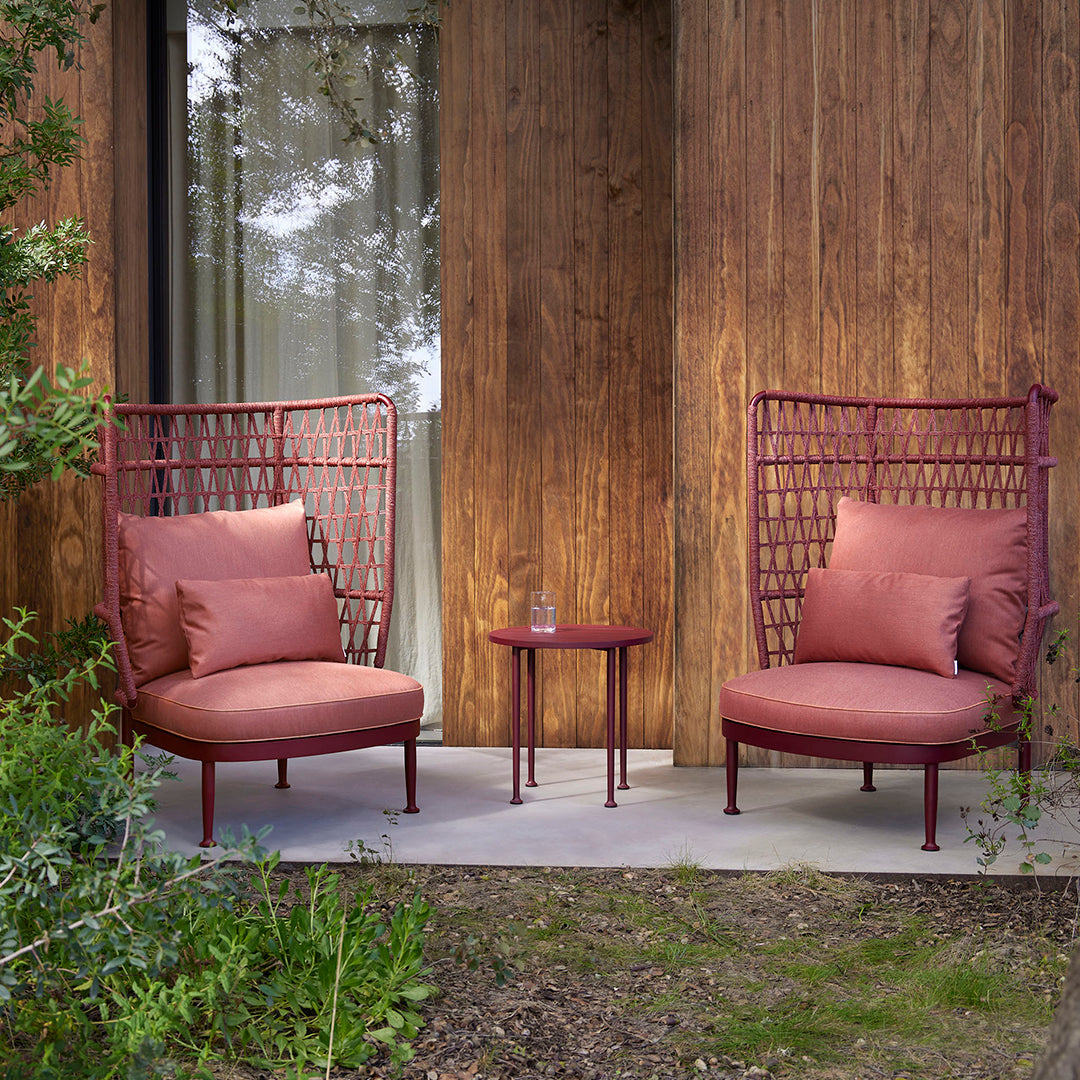 "Rust-colored outdoor chairs with geometric patterns and a matching round table, set against a wooden backdrop."