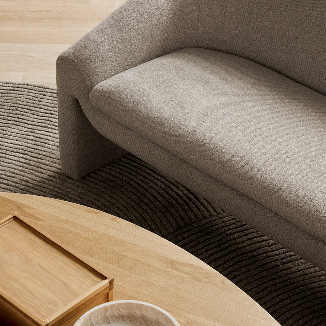 Gray textured couch atop a dark, ridged rug, complemented by a wooden coffee table and round stone bowl.