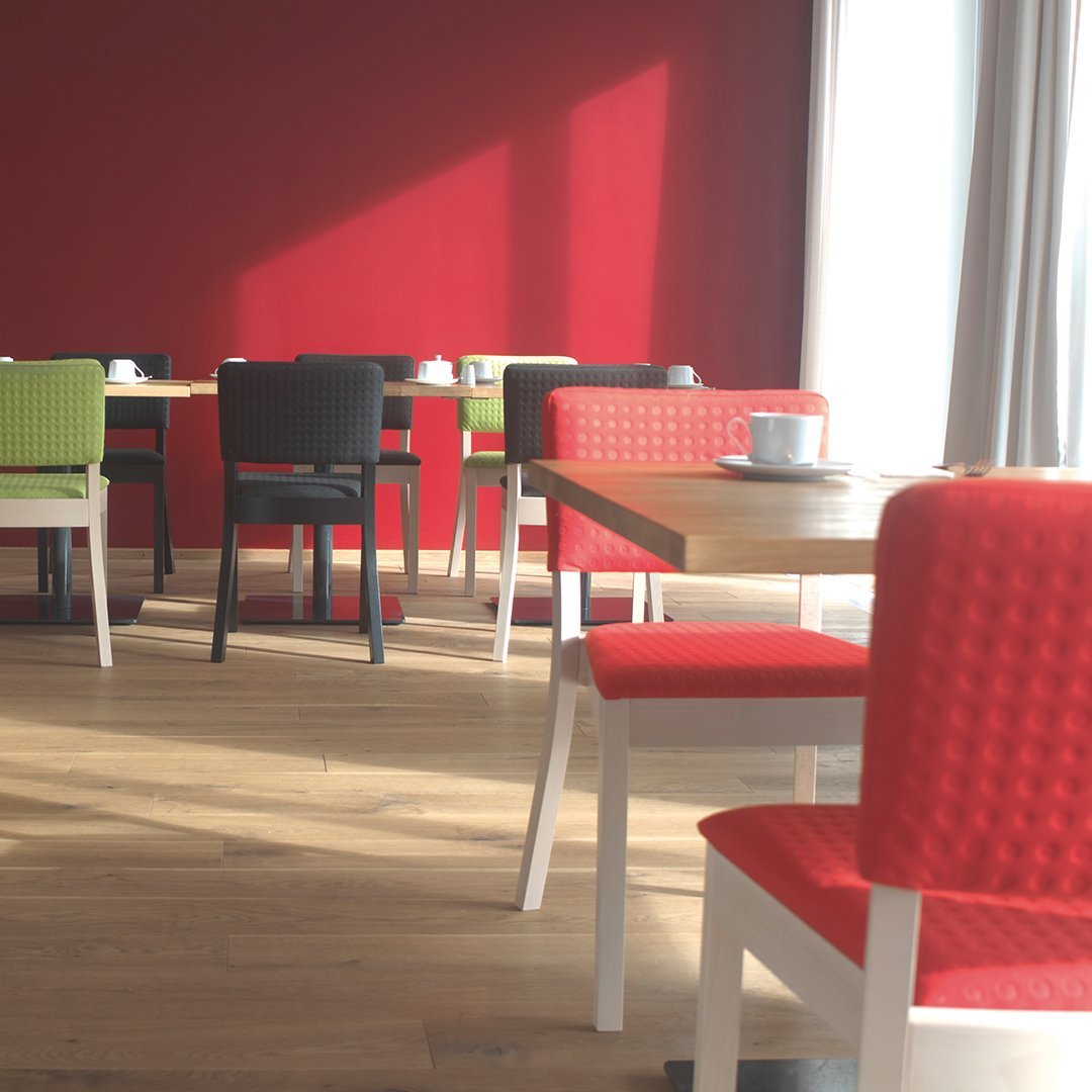 Colorful dining area featuring red, green, and black chairs with textured patterns and white table legs. Bright and inviting.