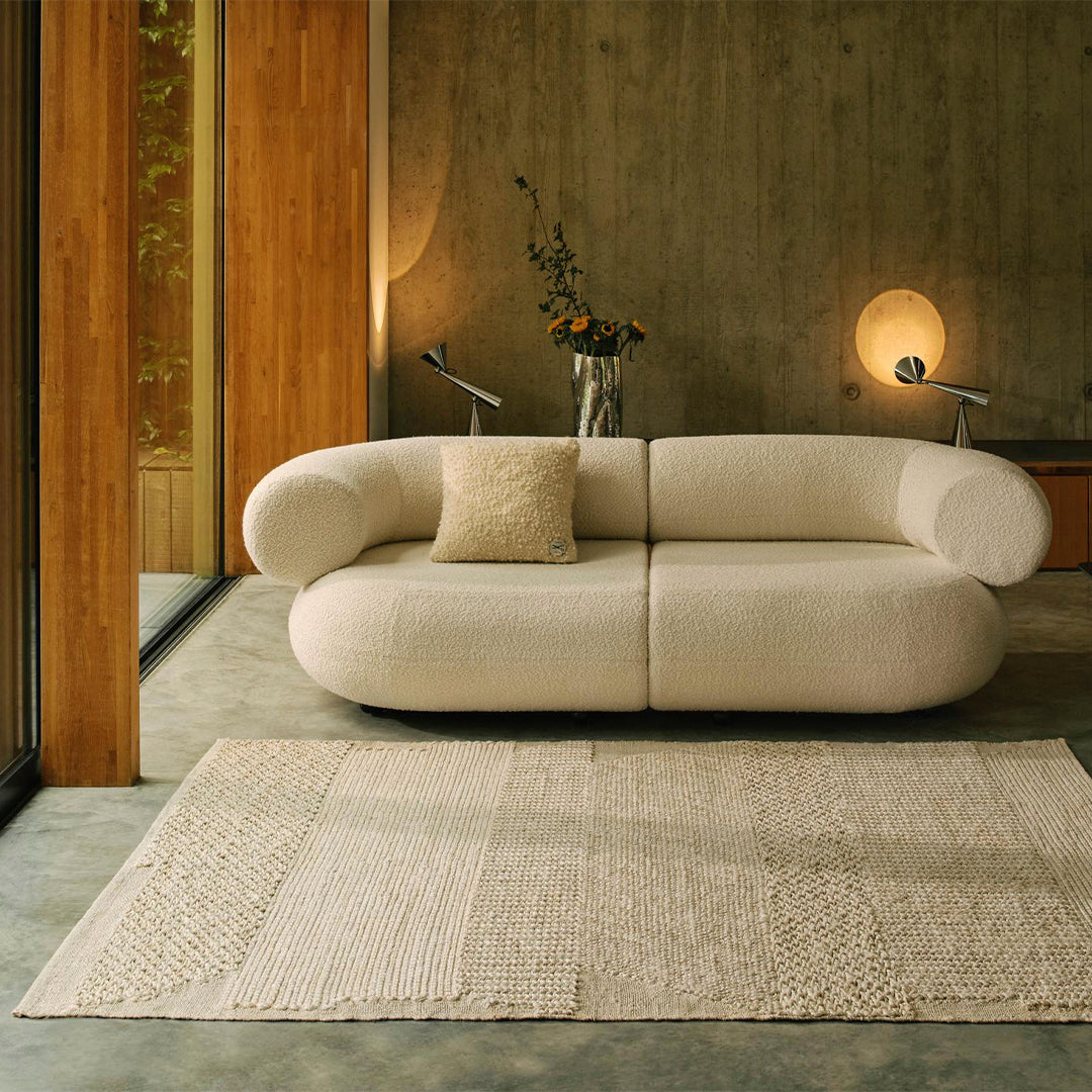 Cream upholstered sofa with textured fabric and a light beige patterned rug in a modern, minimalist setting.