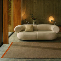 Cream-colored sofa with a textured finish, accompanied by a tan and orange striped rug in a modern setting.